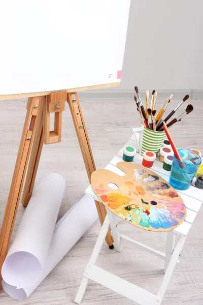 Wooden easel with clean paper and art supplies in room — Stock Photo, Image