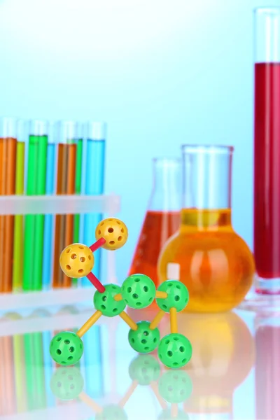 Molecule model and test tubes with colorful liquids on blue background — Stock Photo, Image