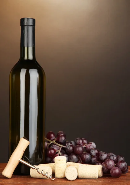 Вино и пробки на деревянном столе на коричневом фоне — стоковое фото