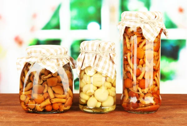 Delicious marinated mushrooms in glass jars, on wooden table on bright background — Stock Photo, Image