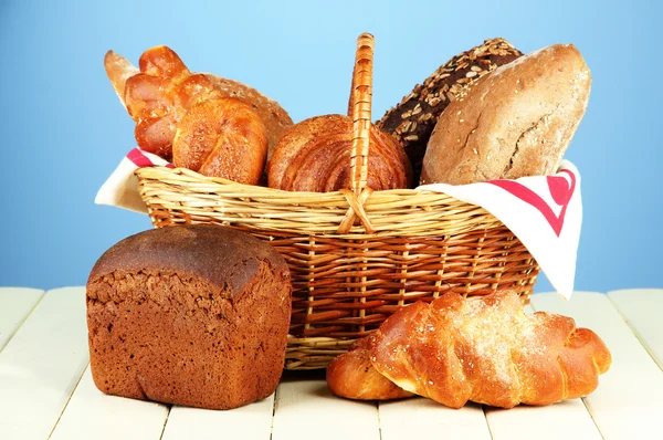 Composizione con pane e panini, in cesto di vimini su tavolo di legno, su sfondo a colori — Foto Stock