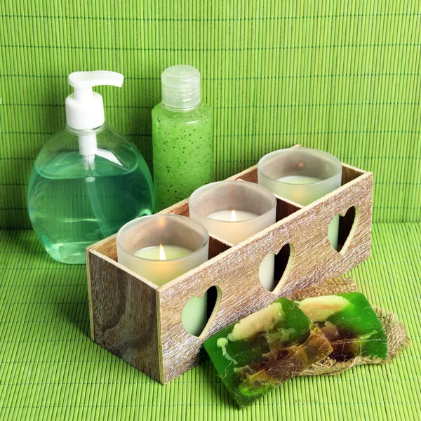 Candles in wooden candlestick, cosmetics bottles and soap, on green bamboo mat — Stock Photo, Image