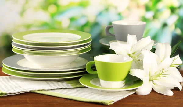 Empty plates and cups on wooden table on green background — Stock Photo, Image