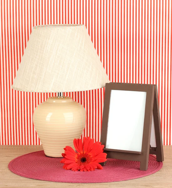 Marco de fotos marrón y lámpara sobre mesa de madera sobre fondo de pared rayado rojo —  Fotos de Stock