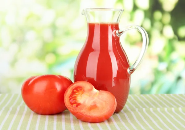 Tomato juice in pitcher on table on bright background — Stock Photo, Image