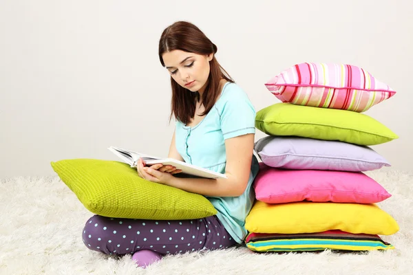 Schönes junges Mädchen mit Kissen und Buch im Zimmer — Stockfoto