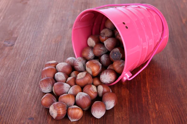 Overturned bucket with hazelnuts on wooden background — Stock Photo, Image