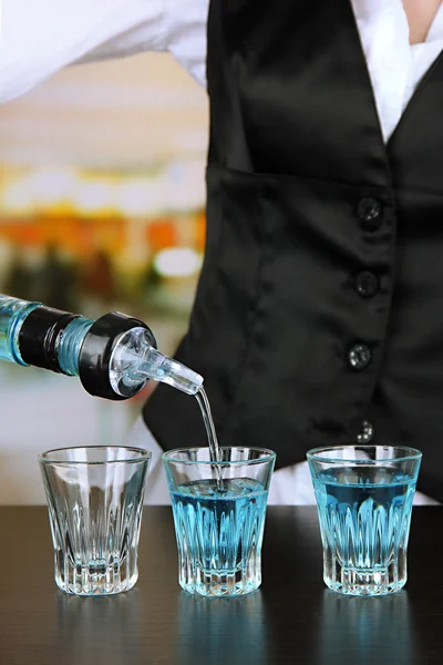 Barmen hand with bottle pouring beverage into glasses, on bright background — Stock Photo, Image