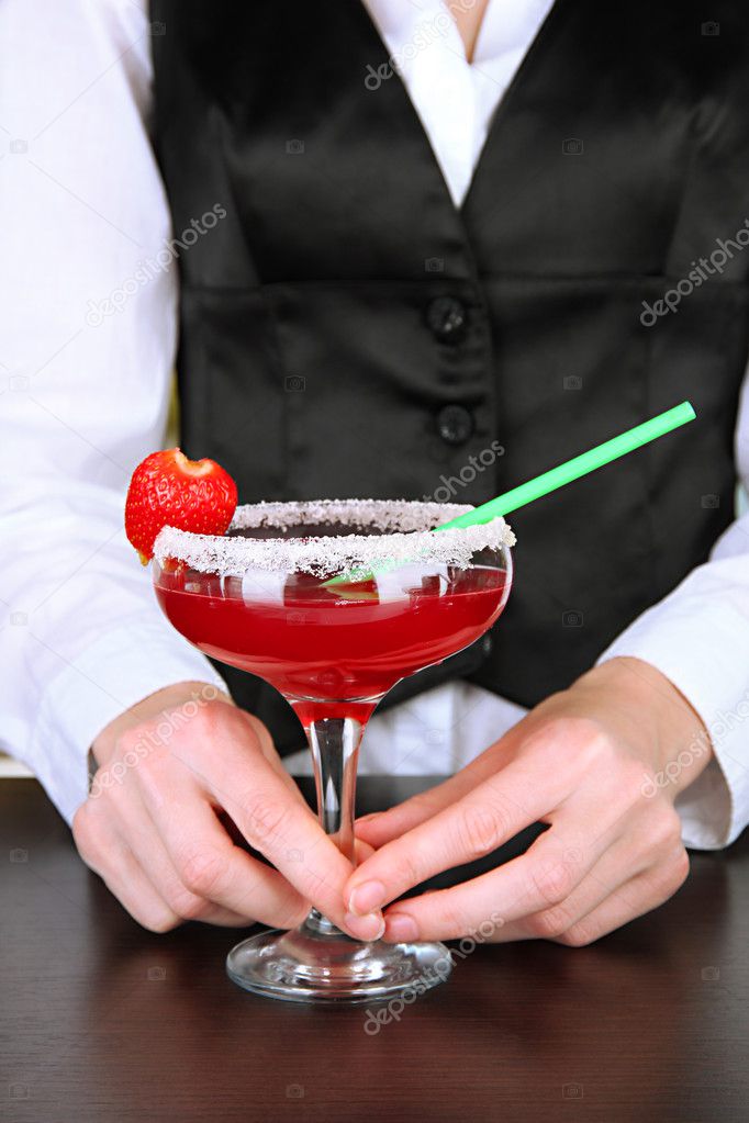 Barmen hand with shaker pouring cocktail into glass, on close up