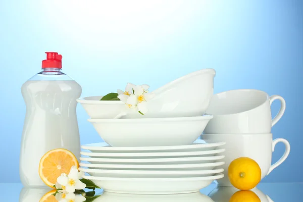 Lege schoon borden en kopjes met afwassen vloeibare en citroen op blauwe achtergrond — Stockfoto