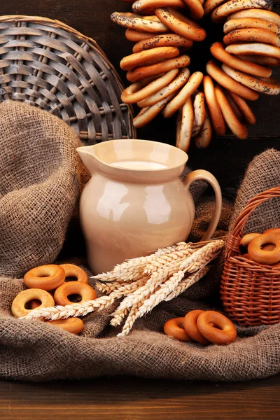 Jar of milk, tasty bagels and spikelets on wooden background — Stock Photo, Image