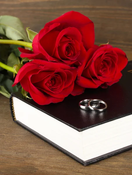 Anillos de boda en la biblia con rosas sobre fondo de madera — Foto de Stock