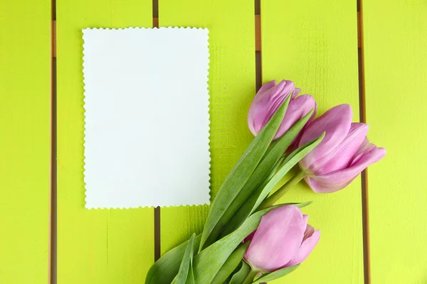Beautiful bouquet of purple tulips and blank card on green wooden background — Stock Photo, Image
