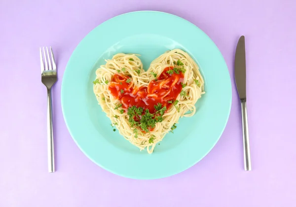 Kokt spaghetti noggrant ordnade i hjärta form och toppad med tomatsås, på färgbakgrund — Stockfoto