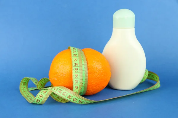 Orange with measuring tape and body cream, on color background — Stock Photo, Image