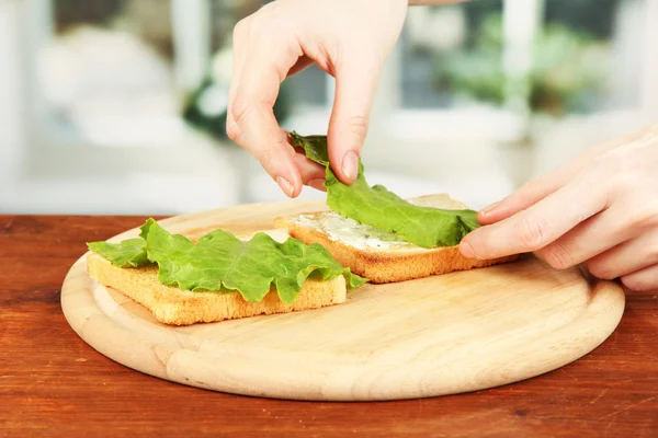 Διαδικασία εκπόνησης σαλάμι ρολά στο ψητό ψωμί, σε φωτεινό φόντο: γυναικείο χέρι βάζει φύλλα σαλάτα με ψητό ψωμί — Φωτογραφία Αρχείου
