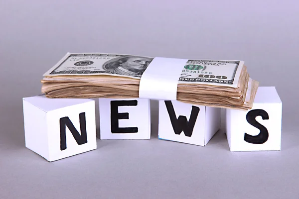 White paper cubes labeled "News" with money on grey background — Stock Photo, Image