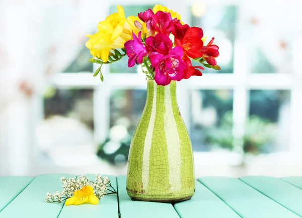 Beautiful bouquet of freesia in yellow vase on wooden table on window background — Stock Photo, Image