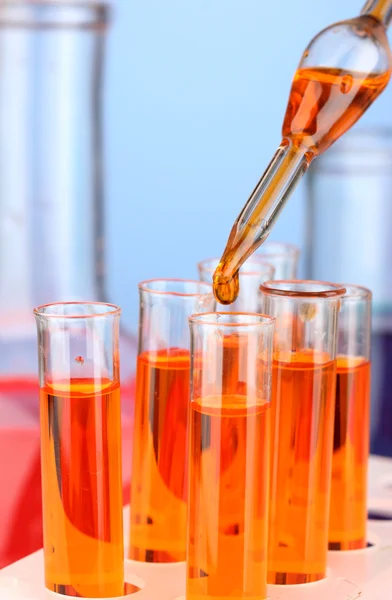 Pipeta de laboratorio con gota de líquido de color sobre tubos de ensayo de vidrio, primer plano — Foto de Stock