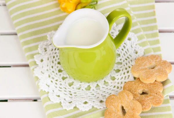 Green jug with milk and cookies on wooden picnic table close-up — Stock Photo, Image
