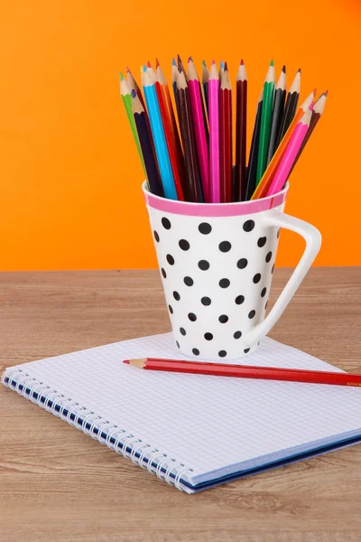 Kleurrijke potloden in cup op tabel op oranje achtergrond — Stockfoto