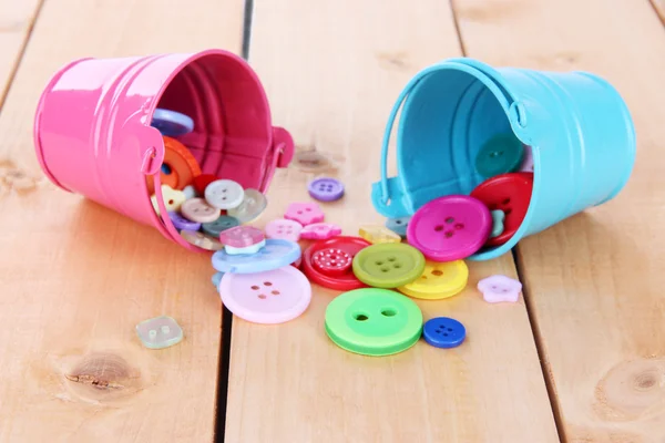 Colorful buttons strewn from buckets on wooden background — Stock Photo, Image