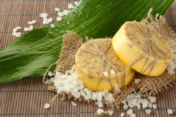 Jabón, sal marina y hojas hechas a mano sobre estera de bambú gris —  Fotos de Stock