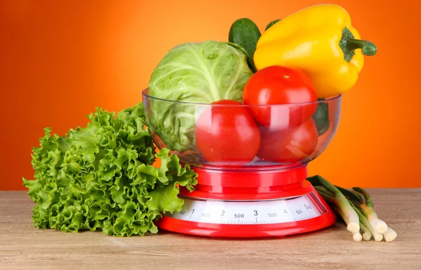 Fresh vegetables in scales on table on orange background — Stock Photo, Image