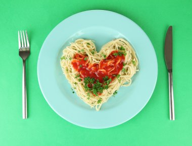 dikkatli bir şekilde kalp şeklinde düzenlenmiş ve renkli arka plan üzerinde domates soslu tepesinde pişmiş spagetti