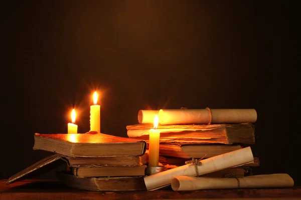 Pile of old books with candle and scroll in dark — Stock Photo, Image