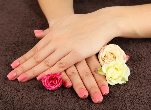 Kvinnelige hender med rosa manikyr og blomster, på farget bakgrunn – stockfoto
