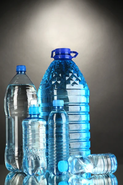 Różne butelki wody na szarym tle — Zdjęcie stockowe