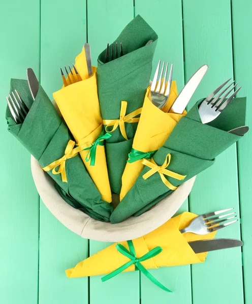 Forks and knives wrapped in green and yellow paper napkins, on color wooden background — Stock Photo, Image