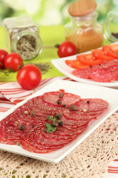 Välsmakande salami på tallrikar på träbord på naturliga bakgrund — Stockfoto