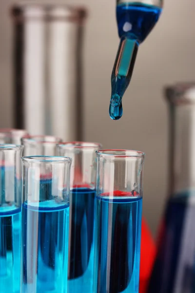 Pipeta de laboratorio con gota de líquido de color sobre tubos de ensayo de vidrio, primer plano — Foto de Stock