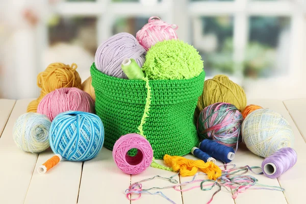 Colorful yarn for knitting in green basket on wooden table on window background — Stock Photo, Image