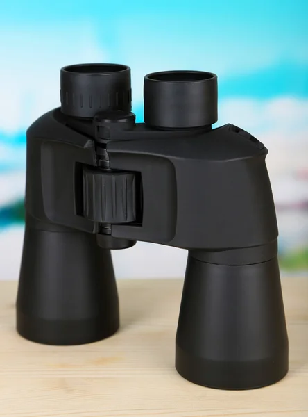 Black modern binoculars on wooden table on blue background — Stock Photo, Image