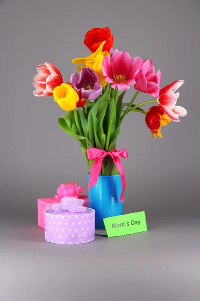 Schöne Tulpen im Strauß mit Geschenken und Notiz auf grauem Hintergrund — Stockfoto