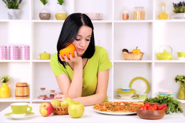 Mooi meisje selecteert pizza of dieet op keuken achtergrond — Stockfoto