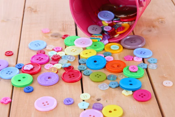 Colorful buttons strewn from bucket on wooden background — Stock Photo, Image