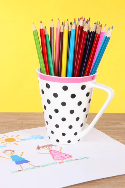 Buntstifte in Tasse auf Tisch auf gelbem Hintergrund — Stockfoto