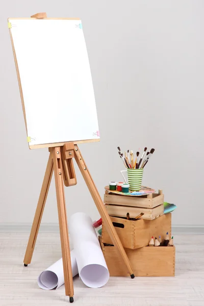 Wooden easel with clean paper and art supplies in room — Stock Photo, Image