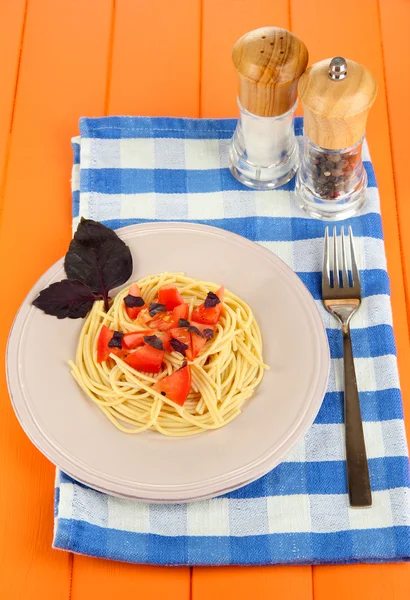 Espaguete com tomates e folhas de manjericão em guardanapo no fundo de madeira — Fotografia de Stock