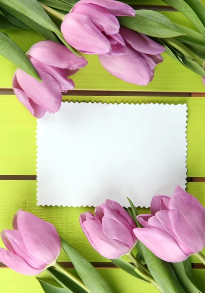 Beautiful bouquet of purple tulips and blank card on green wooden background Royalty Free Stock Images