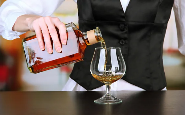 Barman hand with bottle of cognac pouring drink into glass, on bright background — Stock Photo, Image