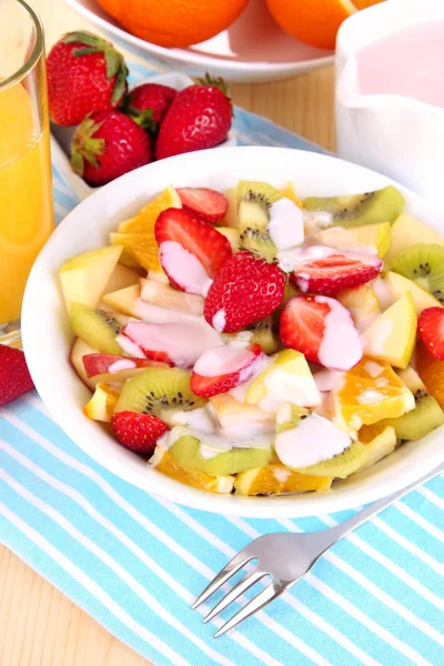 Nyttig fruktsallad med färsk frukt och bär i skål på servett på träbord närbild — Stockfoto