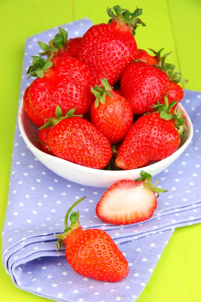 Verse aardbeien in kom op groene houten achtergrond — Stockfoto