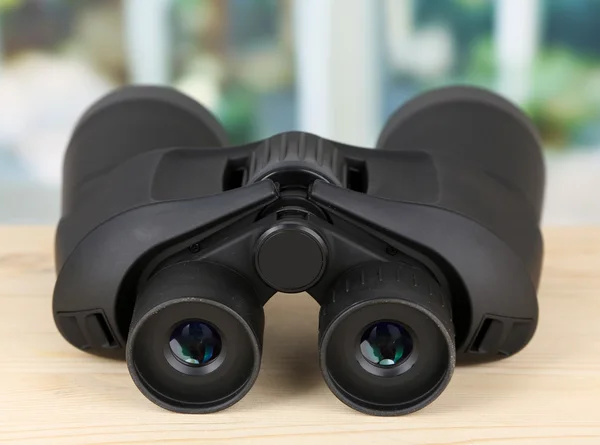 Black modern binoculars on wooden table on window background — Stock Photo, Image