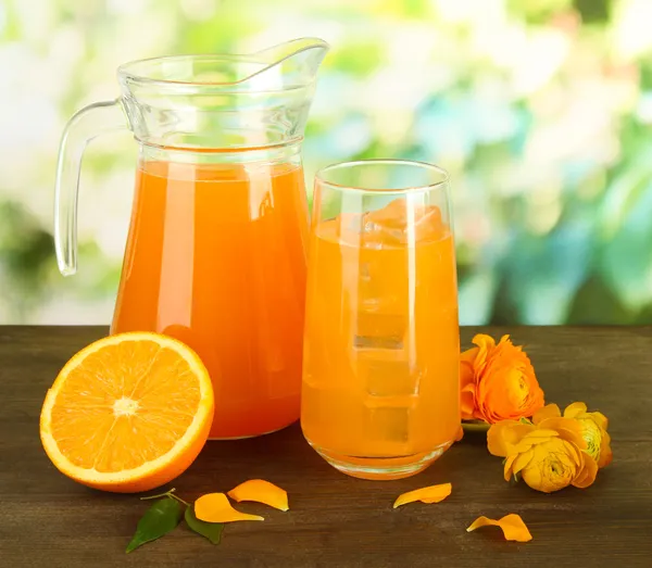 Glas en werper sinaasappelsap op houten tafel, op groene achtergrond — Stockfoto