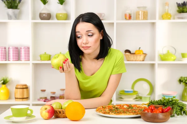 Pretty girl selects pizza or diet on kitchen background — Stock Photo, Image